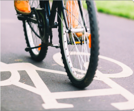 Close-up of front wheel of orange bicycle on a bicycle lane with white painted symbols on asphalt, background with grass.