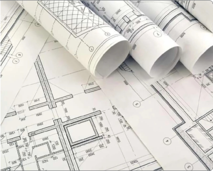 Several rolled-up and flat architectural blueprints with detailed floor plans and measurements spread out on a surface.