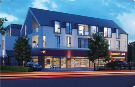 A modern, multi-story building with large windows and a steep dark roof, housing a Sainsbury's Local store on the ground floor. The building is illuminated with streetlights, surrounded by trees and parked cars, with a bright blue evening sky in the background.
